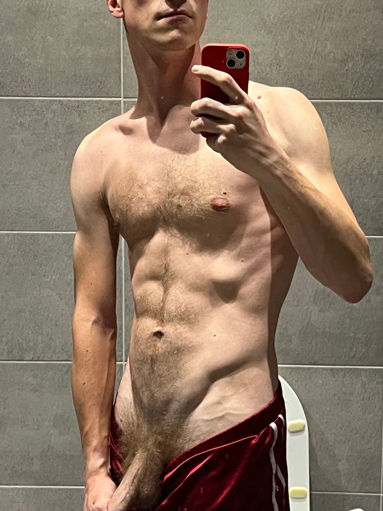 mirror selfie of young, slightly furry blond man stroking his cock in red velvety shorts