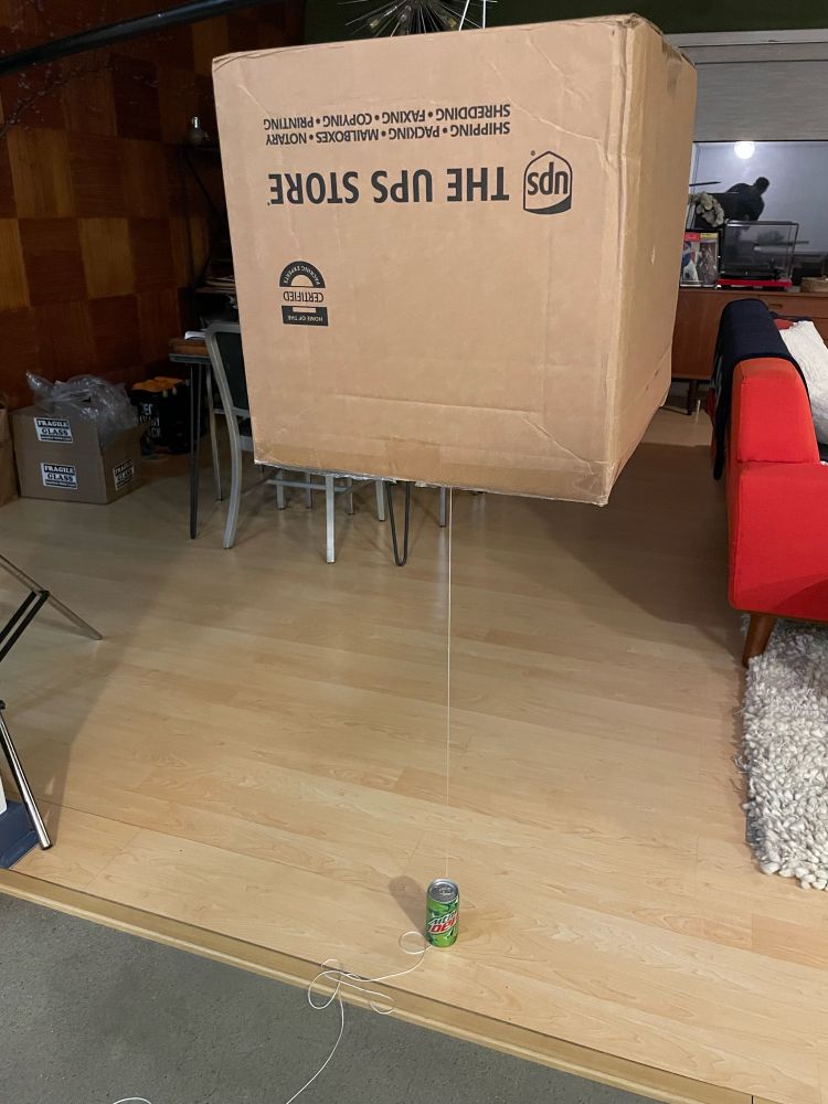 Snapshot of a cardboard box suspended above a small can of Mountain Dew, poised to fall if the can is removed 
