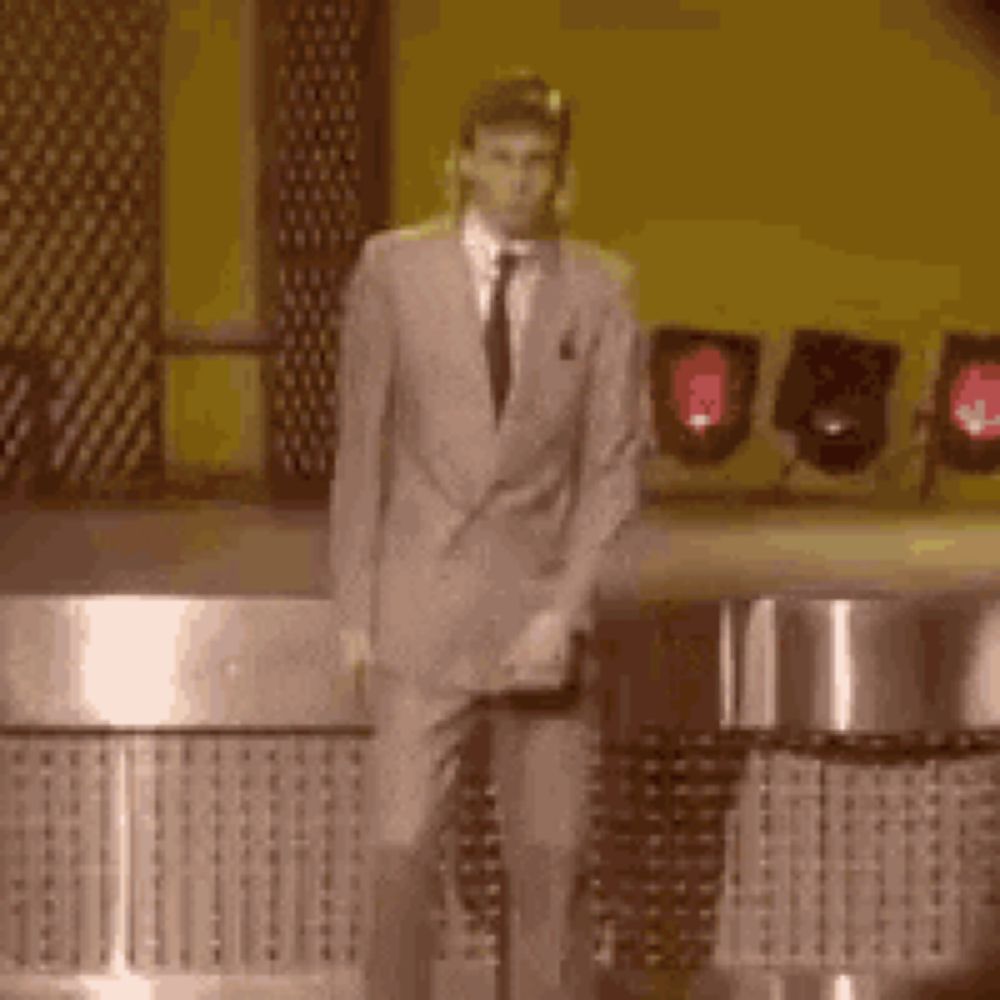 a man in a suit and tie is standing in front of a piano on a stage .