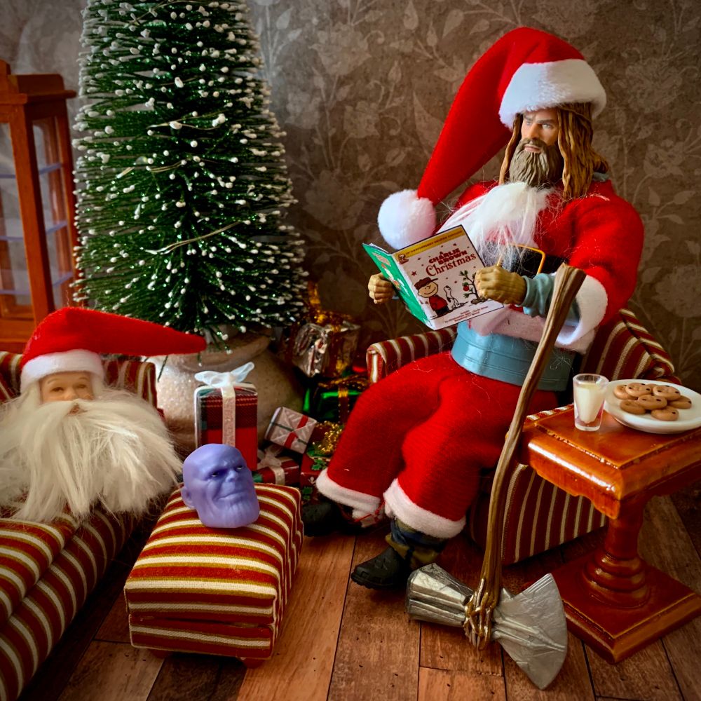 Thor dressed as Santa sits in the living room by the Christmas tree with Thanos and Santa Claus’ heads