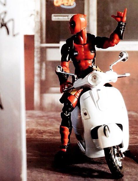 Deadpool on his white scooter waves to Deadshot out of frame 