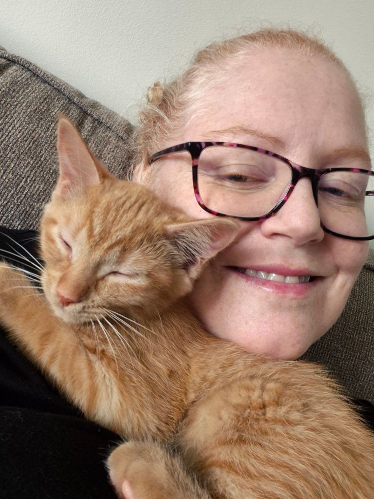 Ginger woman holding a ginger kitten next to her face. 