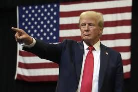 Donald Trump pointing to the right with an american flag behind him