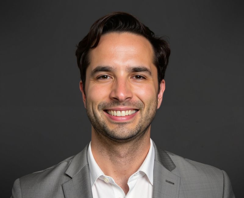 man in gray suit and white shirt smiling against dark gray background
