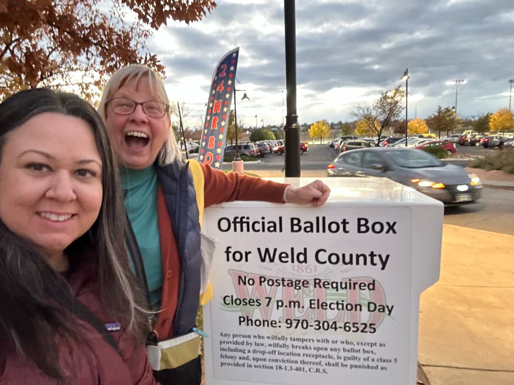 Two voters standing by an outside ballot box looking very happy 