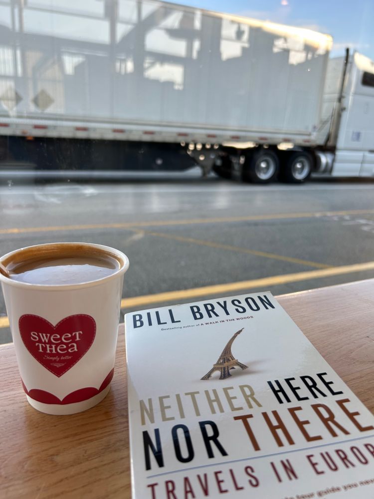 A cup of coffee, a travel book called Neither Here Nor There. Looking out the window at a big truck while I wait at the ferry terminal.