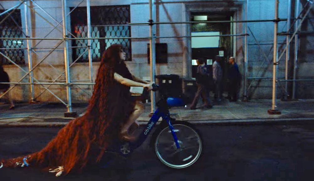 Chappell Road riding a bike share bike wearing a long red wig. 