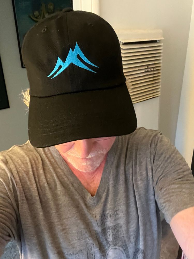 A big nerd wearing a new black baseball cap with an abstract blue logo embroidered on the front. If you know this logo, we should be friends, or we already are. 