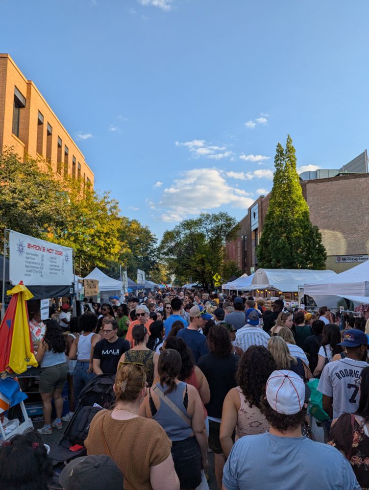Photo of a crowd milling around in a street festival under blue skies 