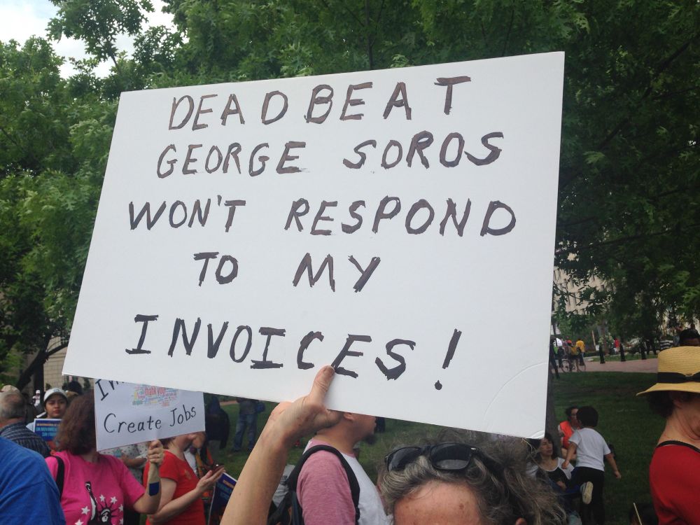 Protest sign reading “Deadbeat George Soros won’t respond to my invoices!”