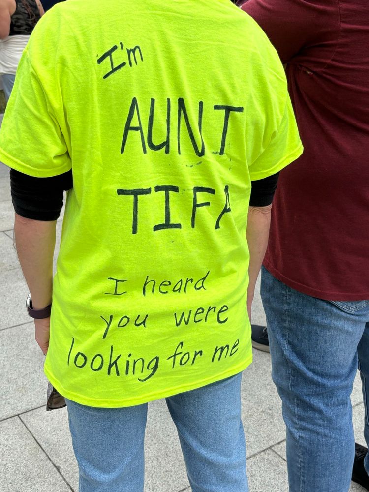 Woman wearing a neon green shirt with text written on the back reading “I’m aunt Tifa. I heard you were looking for me”