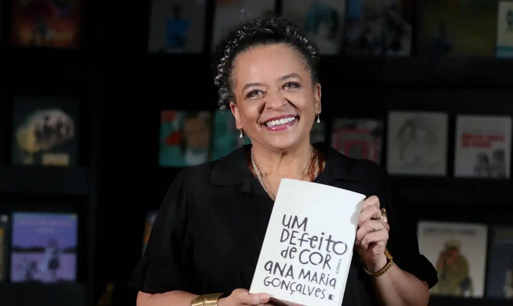 Ana Maria Gonçalves segurando seu livro Um defeito de cor, sorrindo.