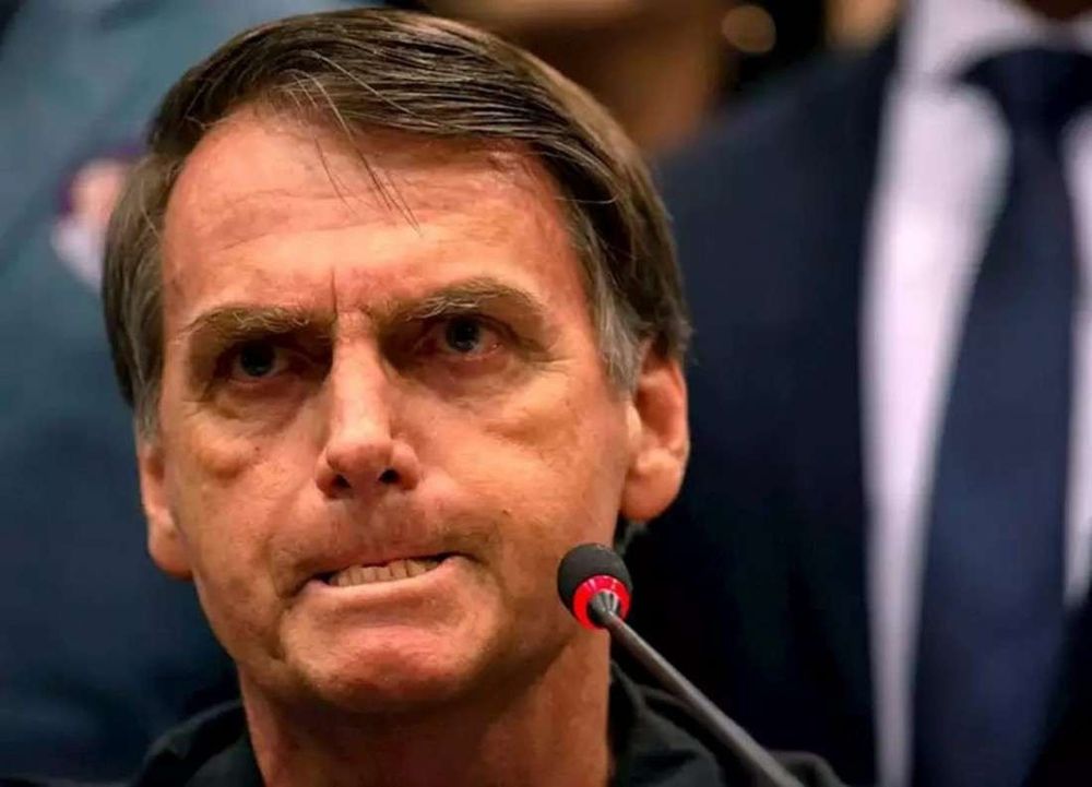 Close de Jair Bolsonaro com expressão tensa, mordendo o lábio inferior e encarando fixamente à frente, como se tentasse segurar um comentário atravessado característico do Constipado