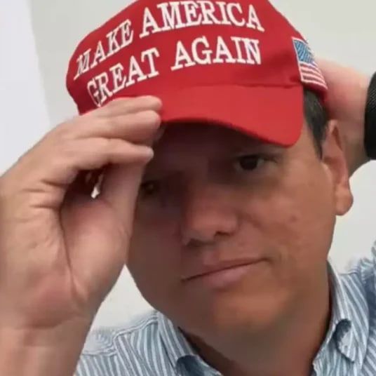 Foto mostra o governador de São Paulo, Tarcísio de Freitas (Republicanos), usando um boné vermelho com a frase “MAKE AMERICA GREAT AGAIN”, slogan de campanha de Donald Trump. Tarcísio segura a aba do boné com uma das mãos, num gesto casual, olhando para a câmera com expressão neutra.