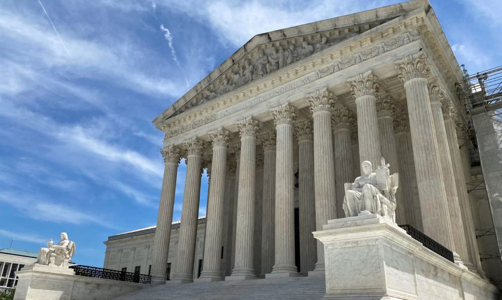 Vista geral do prédio da Suprema Corte dos Estados Unidos, em Washington, com sua fachada neoclássica de mármore branco. A estrutura apresenta oito colunas altas no estilo coríntio, sustentando um frontão triangular decorado com esculturas. A inscrição "Equal Justice Under Law" ("Justiça Igualitária Sob a Lei") está gravada abaixo do frontão. À direita, uma estátua de mármore, conhecida como "Autoridade da Lei", representa uma figura sentada segurando um livro. O céu ao fundo está claro, com nuvens brancas esparsas. Créditos: Will Dunham/Reuters.