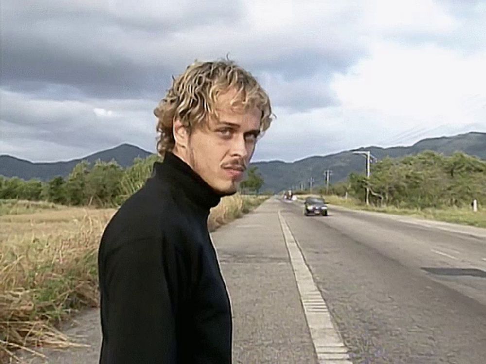 a man in a black turtleneck is standing on the side of the road