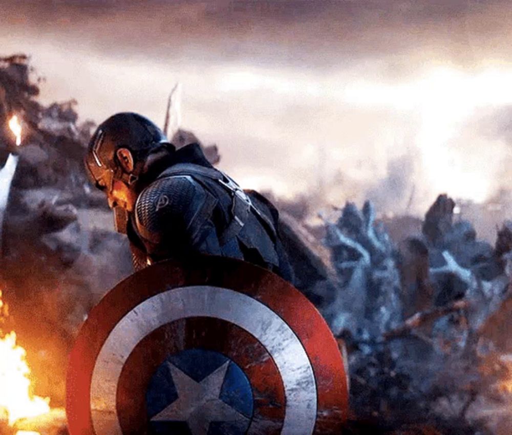 captain america is holding a shield in front of a group of soldiers .