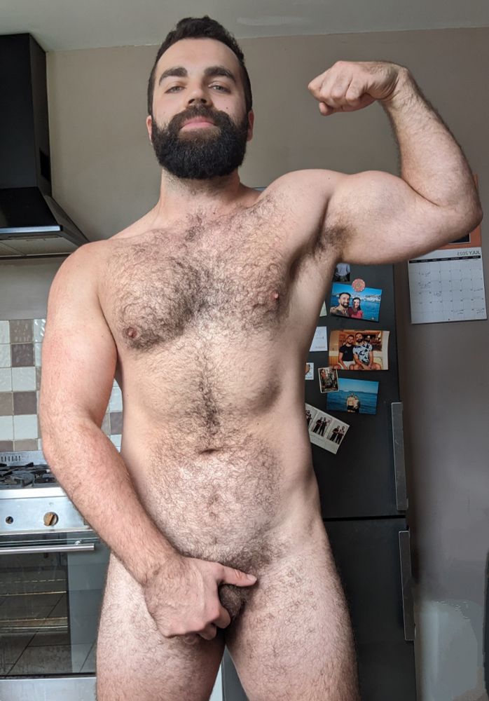 A selfie of me standing naked in the kitchen, flexing my bicep and holding my crotch. 