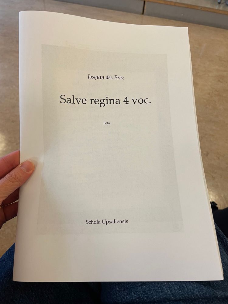 A hand holding a folded pamphlet that says: Josquin des Prez | Salve Regina 4 voc. | Beta | Schola Upsaliensis