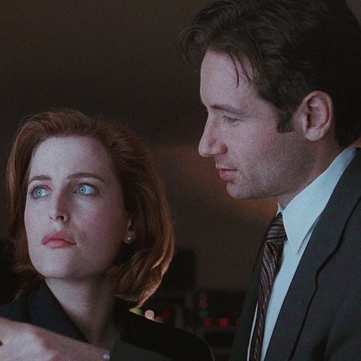 Mulder looks lovingly at Scully, while he points at something off screen. He might be waiting for her reaction to what he is showing her