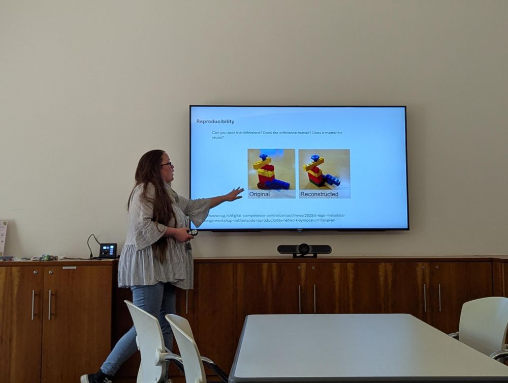 A presenter stands at the front of a room. The presentation slide shows how Lego can be used to demonstrate reproducibility. One image shows the original Lego creation. Next to it is the reconstructed Lego creation showing a few differences from the original. 