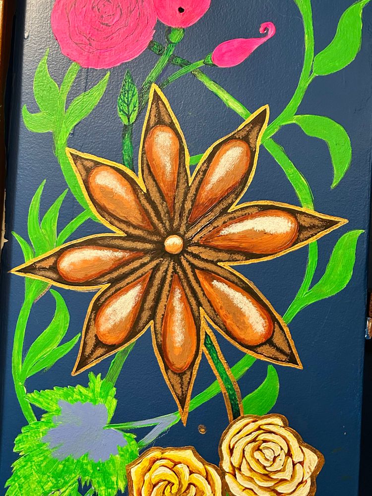 An unfinished painting of greenery and a star anise pod on a dark blue wall. 