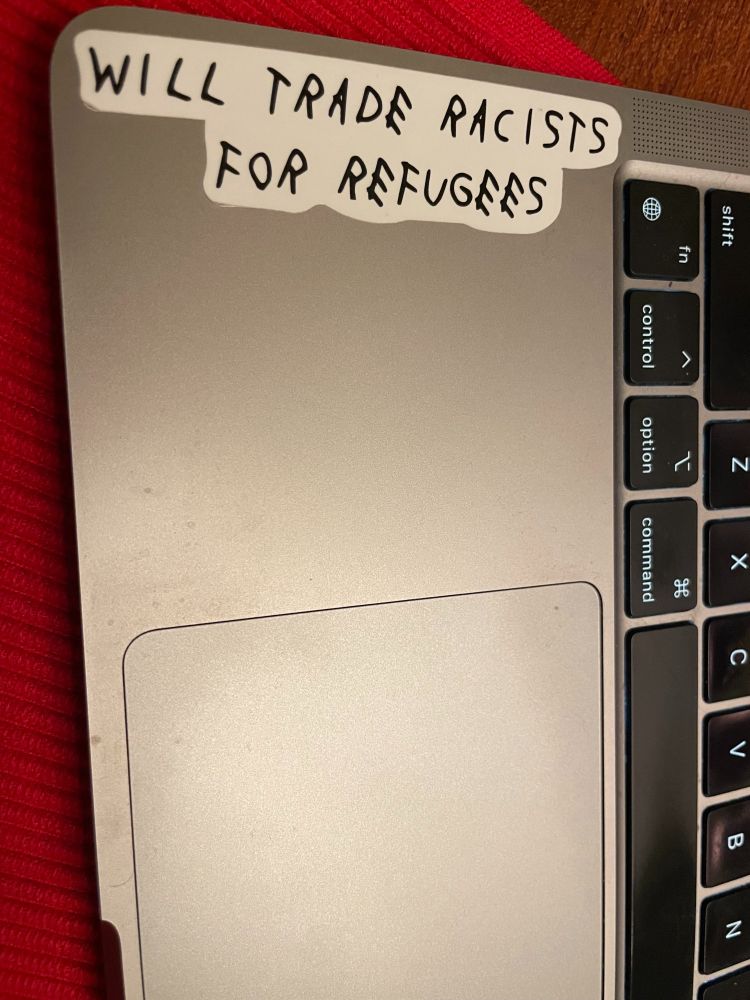Laptop with sticker stating "Will trade racists for refugees." Sticker is from Wear the Peace, founded by the children of refugees.