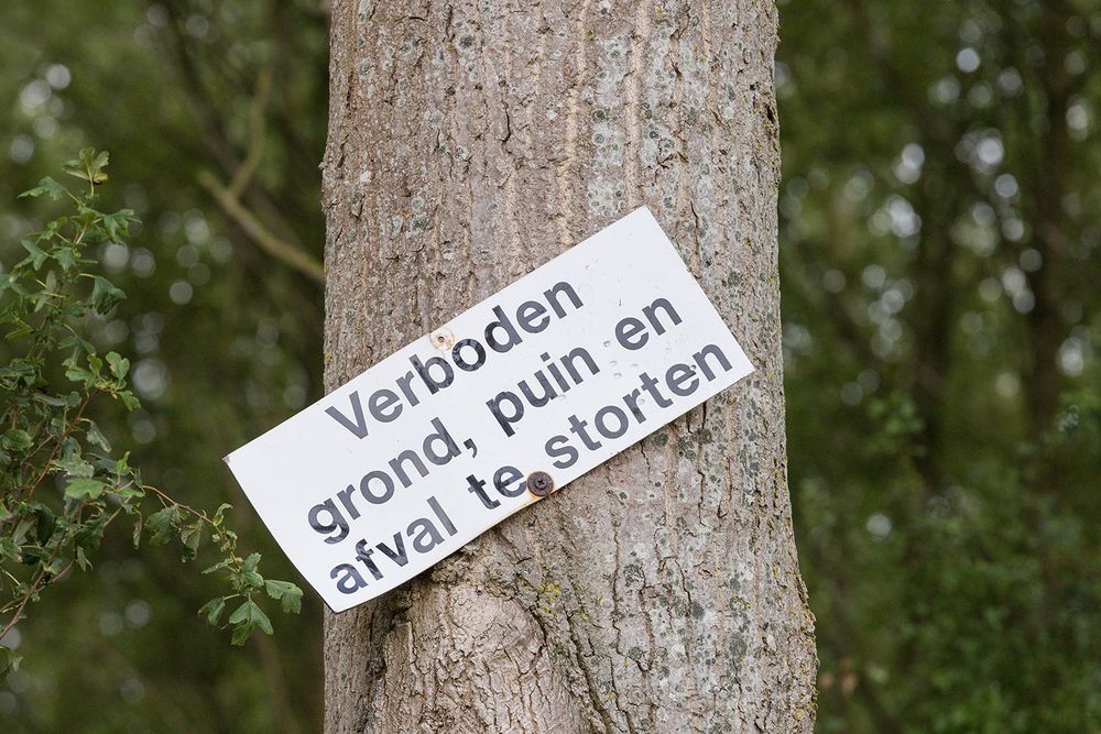 Een aan een boom gemonteerd wit bordje met de tekst: Verboden grond, puin en afval te storten.