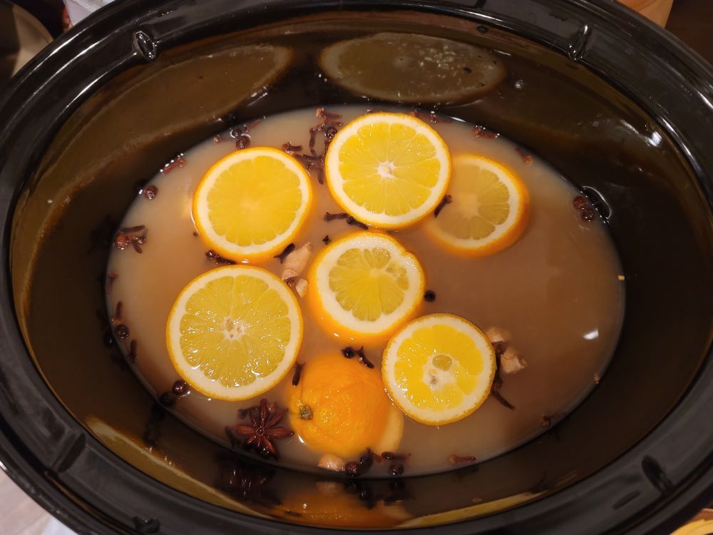 A crockpot full of apple cider, sliced orange, and mulling spices