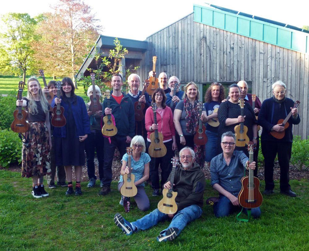 Lots of lovely smiley ukulele players in a park in the early evening sunshine.
