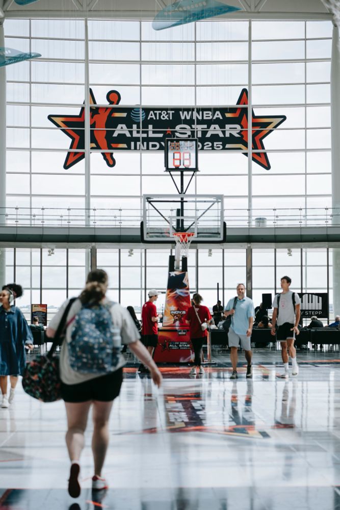 Photo of a basketball hoop set up in the Indianapolis airport. A sign overhead is advertising the WNBA All-Star Game. 