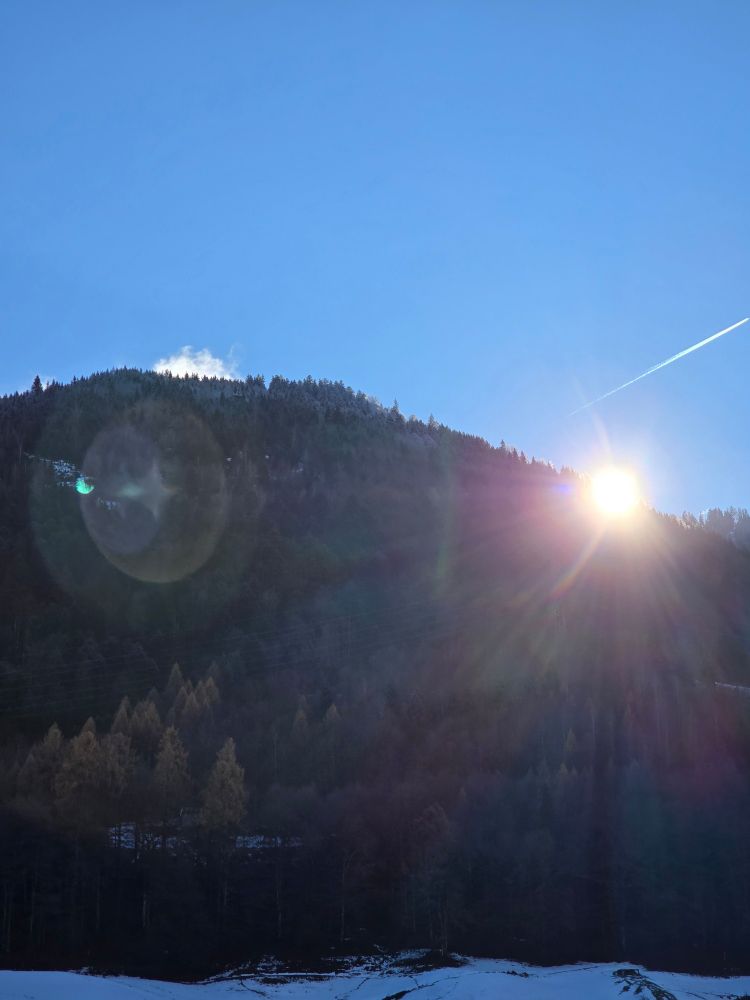 Sun peeking over the mountains,  snow on the ground below