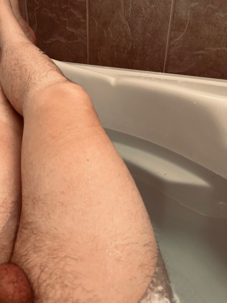 Thick, legs crossed in a bathtub. Partial testicle visible. 