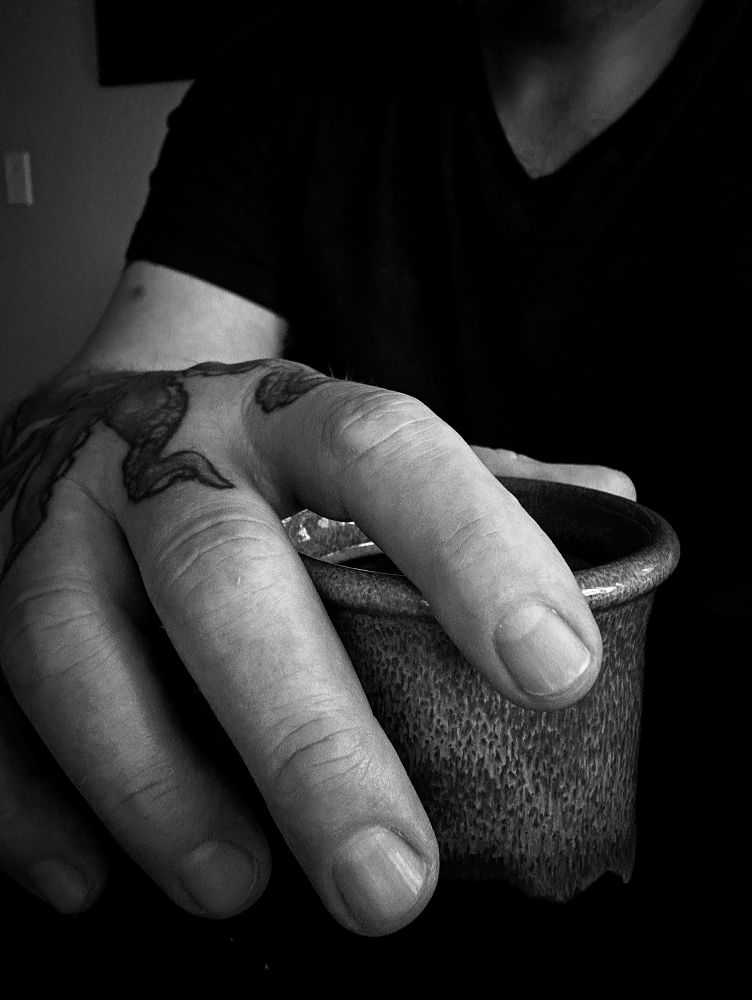 Black and white photo of a man’s hand resting atop a cup of coffee. 