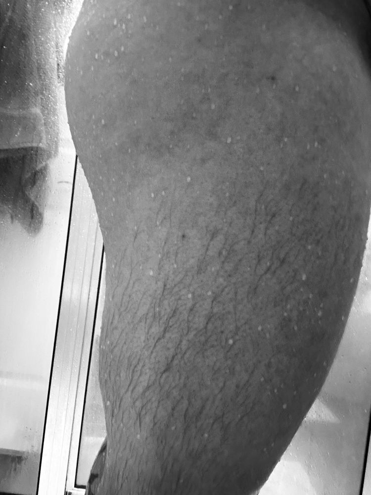 Black and white photo of a man’s thigh and a touch of butt. Taken in a side profile. Man is wet from shower