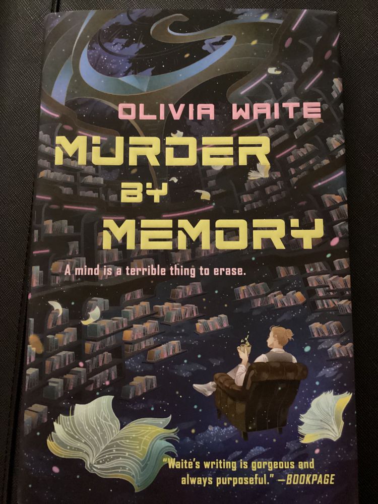 The cover of Murder by Memory by Olivia Waite. A person with their brown hair in a bun sits in an upholstered chair with their back to the viewer. In front of them hover shelves of books against a starscape, while more books flutter around.