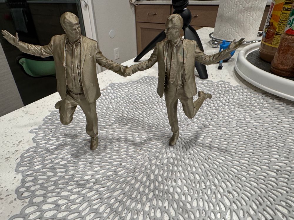 A 3d printed model in gold of the imfamous best friends statue in DC. Orange guy and rich pedophile holding hands