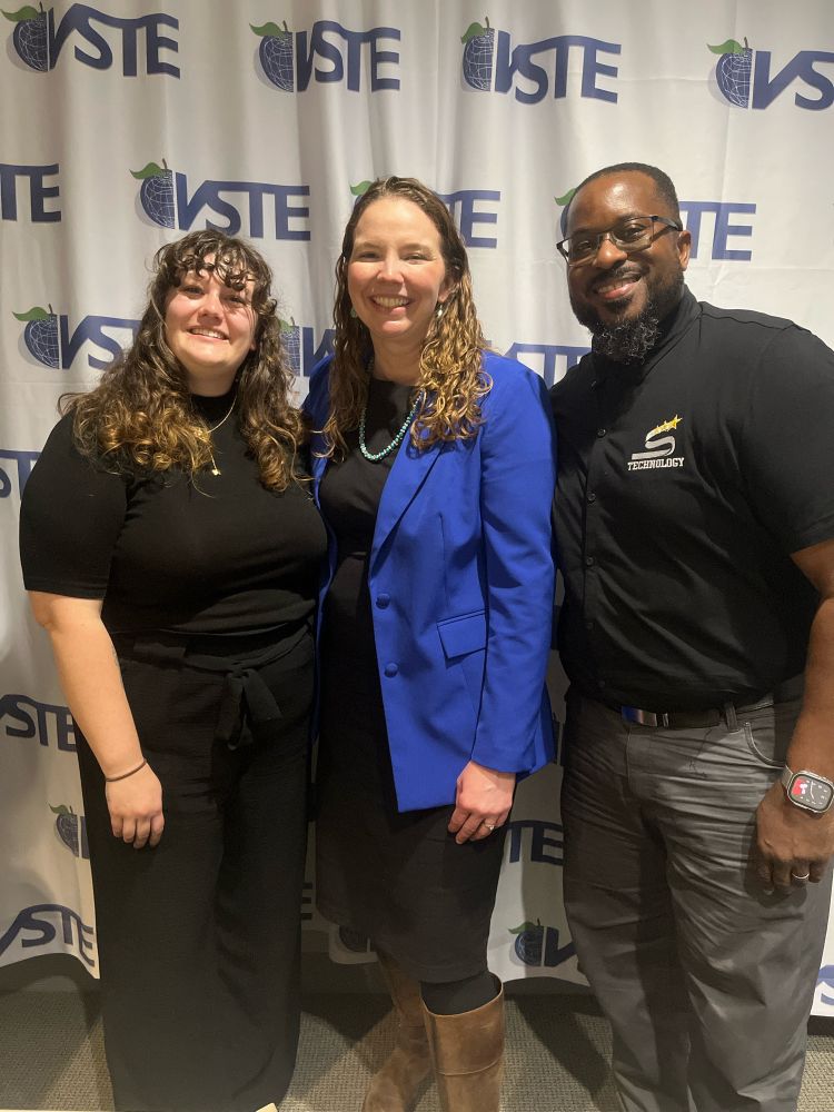 Three presenters smiling and posing in front of VSTE logo backdrop. 
