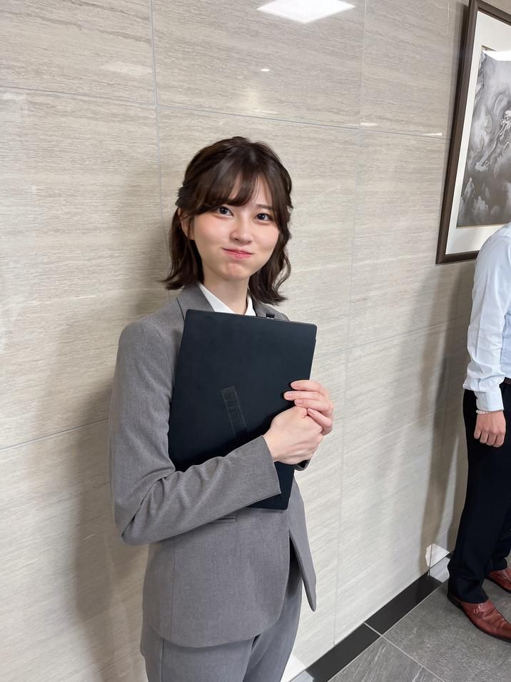 A woman in a grey suit, puffing out her cheeks 