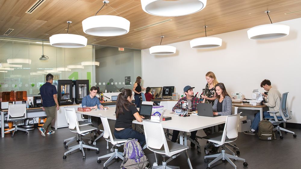 A group of students work at various stations in the Library's Maker Studio. People pictured are sewing, working on robotics, working on laptops, and at a 3d printer. 