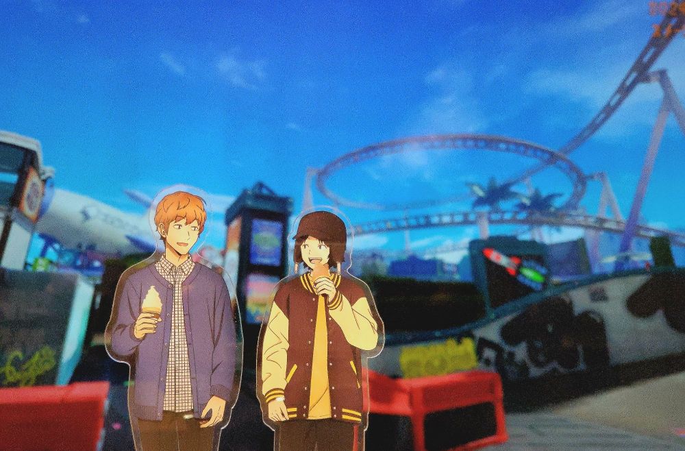 スプラトゥーン3のスメーシーワールドで、飛行機型の建造物とジェットコースターを背景にして並んだ来馬先輩と別役くんのアクリルスタンドの写真