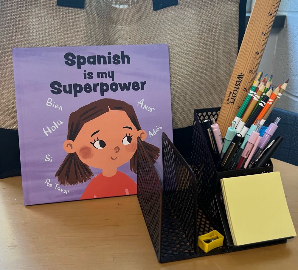 Libro para nińos titulado “Spanish is my Superpower” en una mesa al lado de un envase con lápices y plumas.
