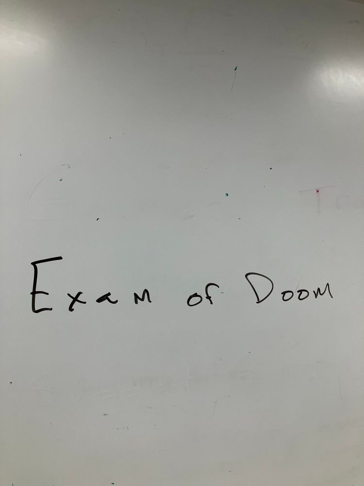 A classroom whiteboard with the phrase Exam of Doom written across it. 