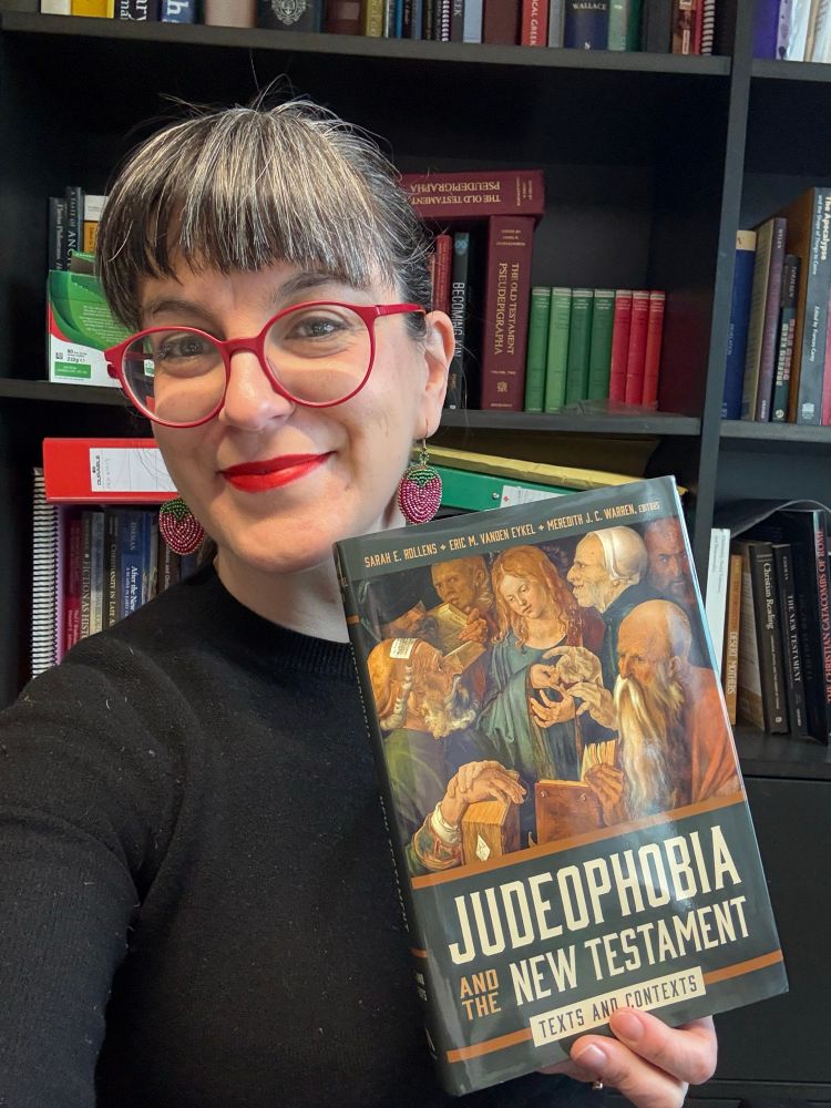 A woman with dark hair and light skin holding a copy of Judeophobia and the New Testament in hardcover. 