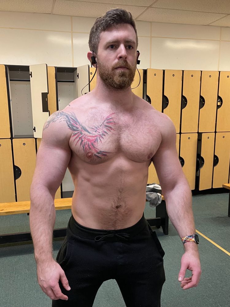 Just a mid lookin dude standing in a locker room without a shirt 
