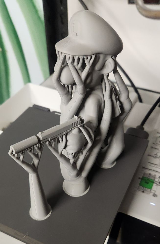 A three d printed model of luigi from the mario brothers, holding a gun with a silencer on the print bed with tree supports all around it