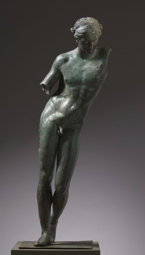 The Apollo Sauroctonos in Cleveland. A Greek or Roman bronze statue of a naked young boy. His left arm is missing entirely, the left arm is preserved to just above the elbow. He's leaning to his left so that his body shows a pronounced curve. The patina of the statue is different shades of dark green.