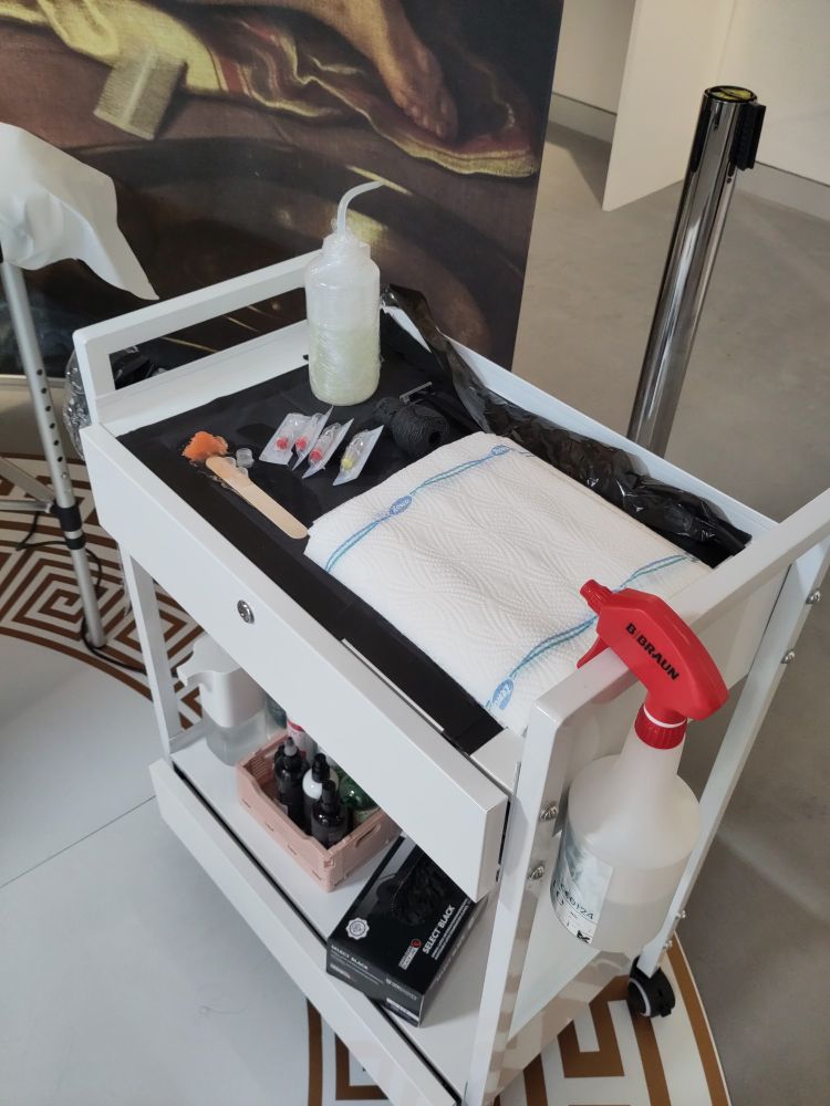 A white metal rolling cart is filled with tattoo supplies.