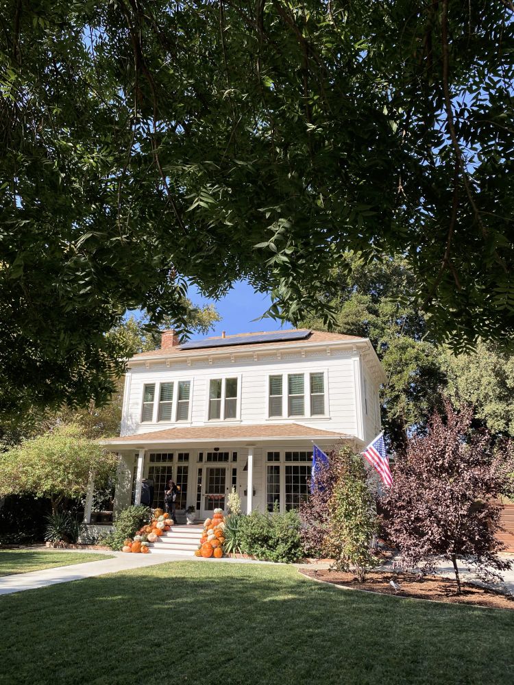 foto de uma casa antiga branca de dois andares com as escadas decoradas com abóboras, um gramado na frente.