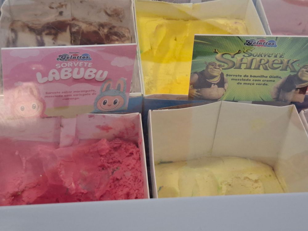 Foto de dois potes de sorvete. Um é rosa e tem uma placa "sorvete labubu" (morangurte) e o outro é verde claro e tem uma placa "sorvete shrek" (maçã verde) 